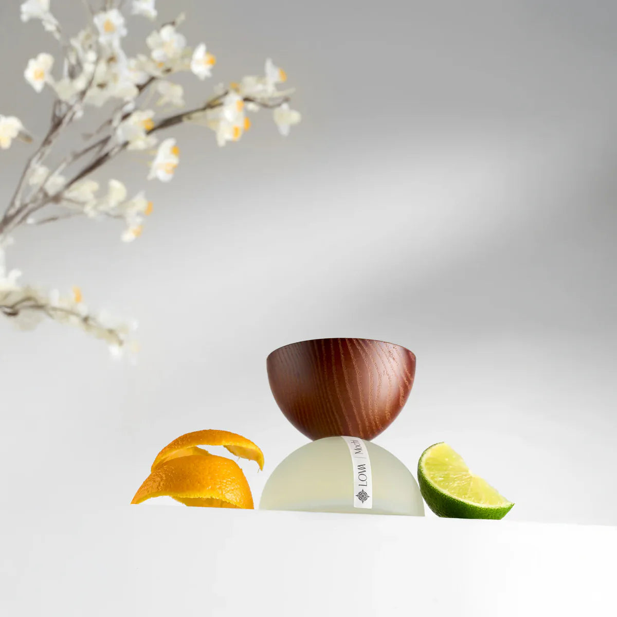 Mochi by LOVA perfume bottle with citrus fruits and white blossoms on light background