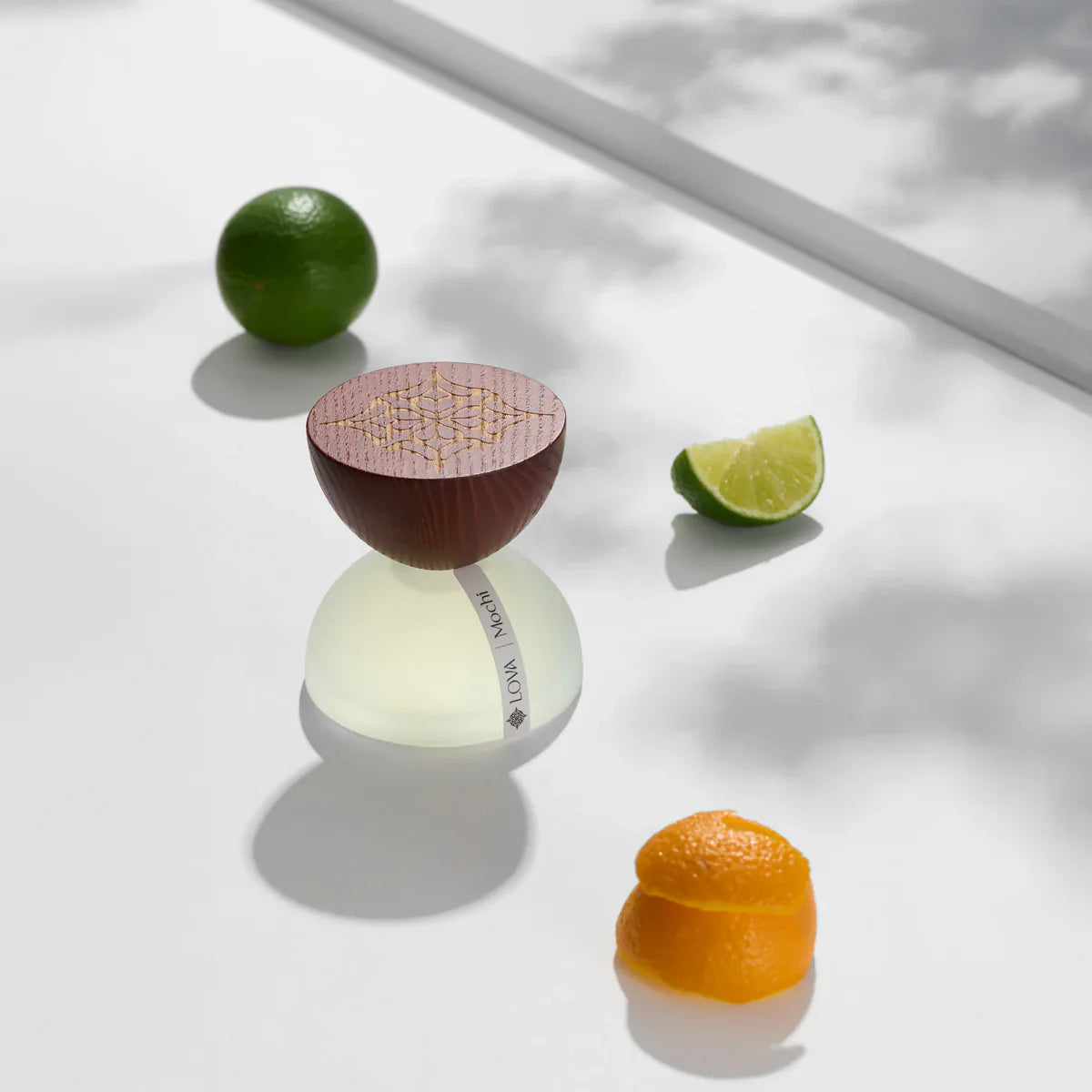 Mochi by LOVA perfume bottle with lime and orange peel on white surface with natural shadows
