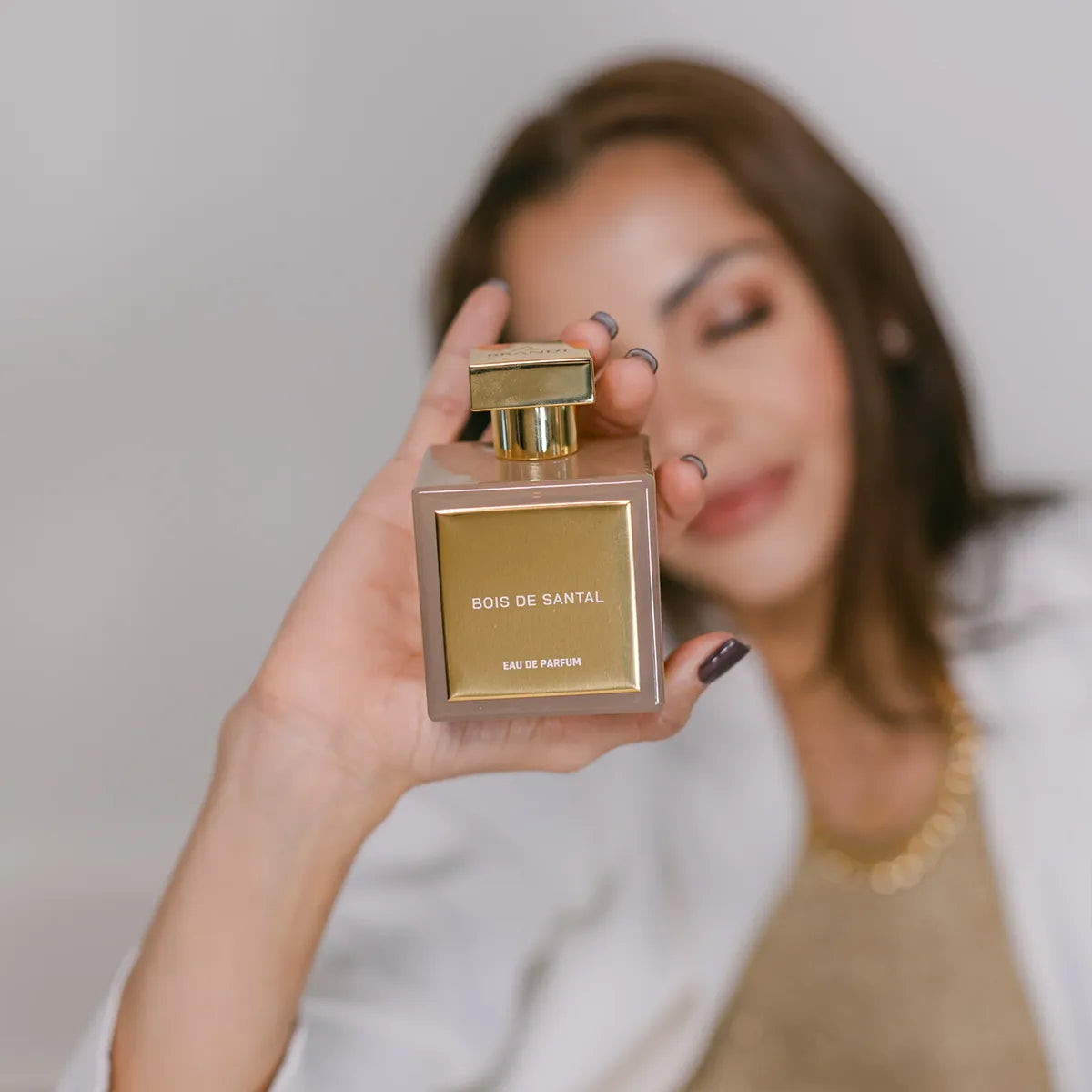 Woman holding a Bois de Santal perfume bottle against a neutral background