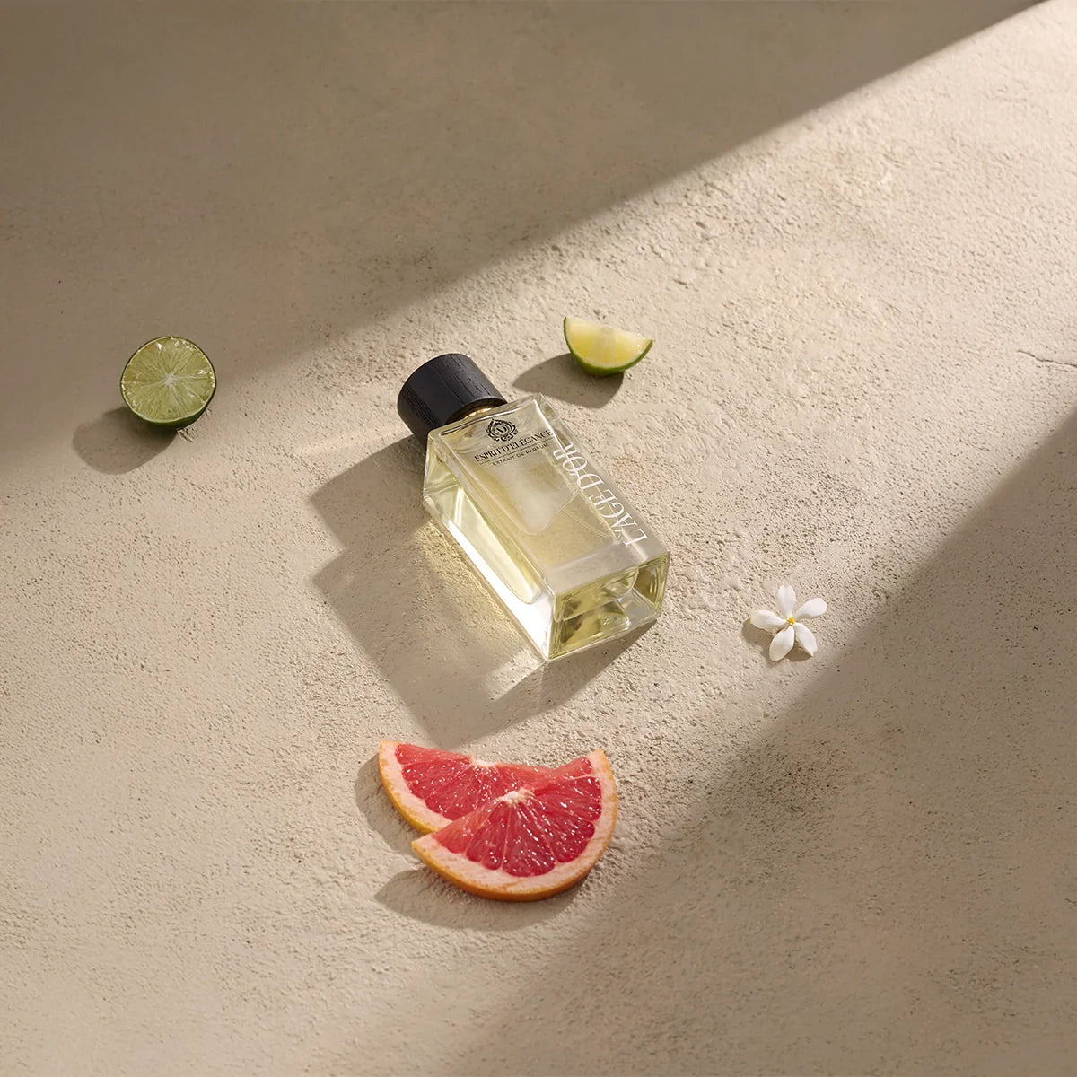 Esprit d’Élégance by L’Âge d’Or luxury perfume bottle styled with grapefruit, lime and white floral accents on beige surface
